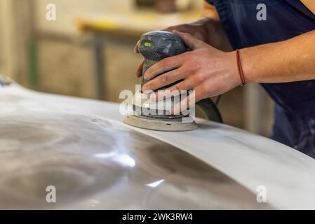 Grinder nelle mani di un uomo che affilare una vernice per auto in auto shop. Foto Stock