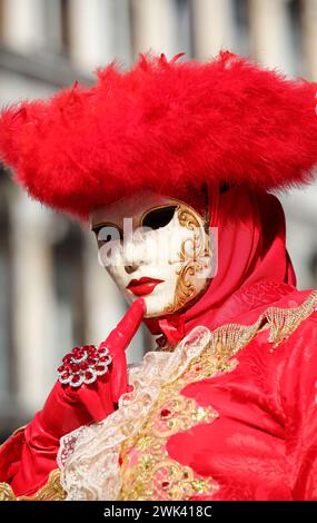 Persona mascherata con il viso coperto da maschera con guanti a mano durante il carnevale di Venezia con l'antico palazzo sullo sfondo Foto Stock