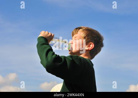 Un ragazzo beve l'acqua da una bottiglia e l'altra mano tiene la palla Foto Stock