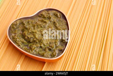 Pesto al basilico in un contenitore a forma di cuore su spaghetti crudi Foto Stock