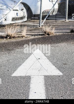 Questa immagine cattura una freccia direzionale bianca che indica il movimento in avanti sulla superficie di una strada asfaltata all'interno di un parcheggio urbano. Il bac Foto Stock