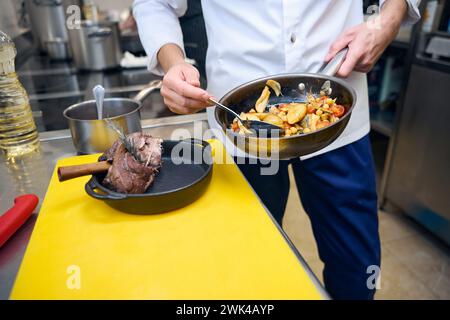 Il dipendente della cucina prepara il gambo di agnello con verdure e salsa per servire Foto Stock