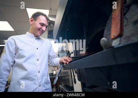 Lo chef sorridente mette in forno una padella con carne Foto Stock