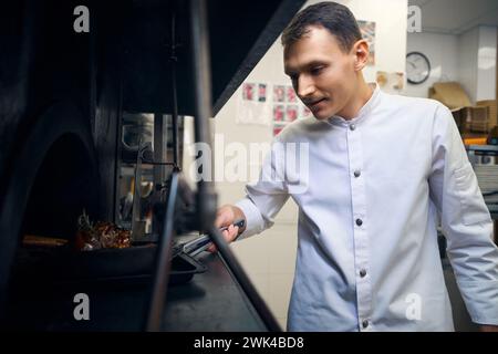 Il giovane chef prepara la padella con la carne del forno Foto Stock