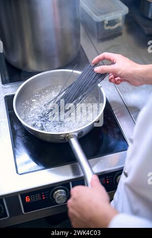 Cook mette una porzione di spaghetti neri in acqua bollente Foto Stock