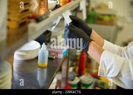 Il lavoratore della cucina con guanti protettivi neri guarda attraverso una ricevuta Foto Stock