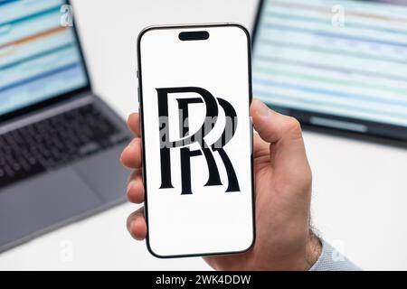 PRAGA, CECHIA - FEBBRAIO 2024: Logo Rolls Royce sullo schermo dello smartphone mans Hand e laptop sullo sfondo Foto Stock