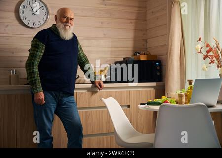 L'uomo anziano in un gilet caldo sta in cucina Foto Stock
