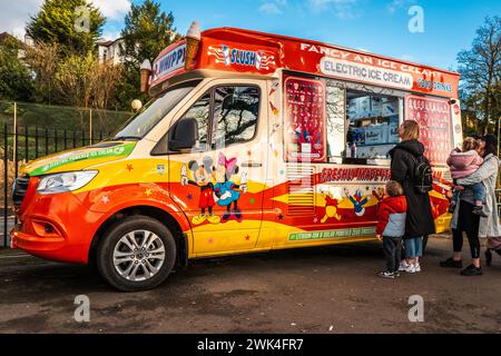 Persone che acquistano gelati da un pulmino elettrico per gelati in un soleggiato pomeriggio invernale. Eco-compatibile, camion elettrico, fornitore, Galles, Cardiff. Foto Stock