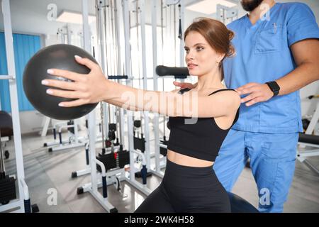 Paziente che fa esercizi con la palla sotto la supervisione di un fisioterapista Foto Stock