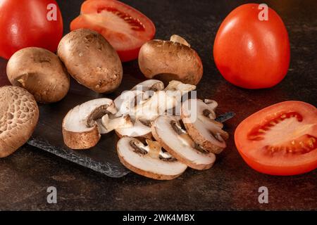 Un mix rustico di pomodori freschi e funghi su un tavolo di legno scuro, ideale per cucinare e mangiare sano. I colori e le trame naturali ma Foto Stock