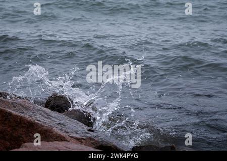 Primo piano dello spruzzo di una piccola onda che si schianta sulle rocce. Foto Stock