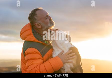 vecchio uomo maturo escursioni in montagna con il suo cane, esercizio fisico e fitness per il benessere, stile di vita sano e sorriso. Faccia di un signore anziano e maturo Foto Stock