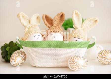 Uova di Pasqua in cappelli a maglia con orecchie di coniglio nel nido. Concetto di festa di Pasqua Foto Stock