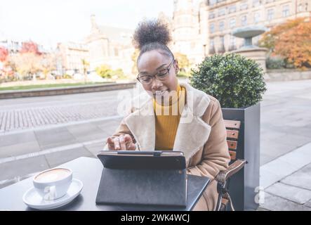 Studentessa africana e learning corso di formazione a distanza studiare lavorare in caffetteria. Giovane donna etnica che guarda il webinar online sull'istruzione utilizzando un notebook. Foto Stock