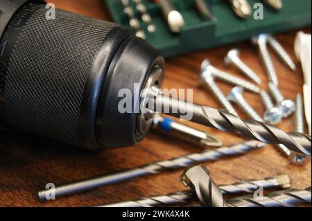 Primo piano di un trapano, set con trapani e vari materiali su fondo in legno. Foto Stock