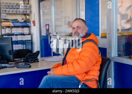 Un uomo che aspetta in garage la manutenzione della sua auto e gli pneumatici invernali montati prima della stagione invernale Foto Stock