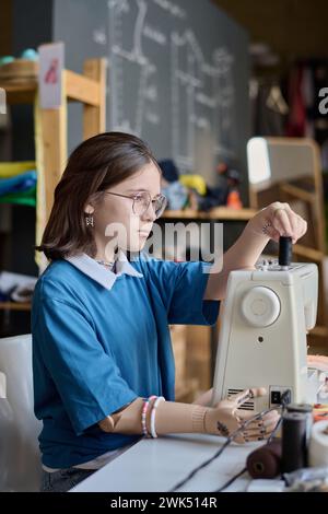 Vista laterale verticale ritratto di adolescente con disabilità che utilizza una macchina da cucire in classe di formazione professionale Foto Stock