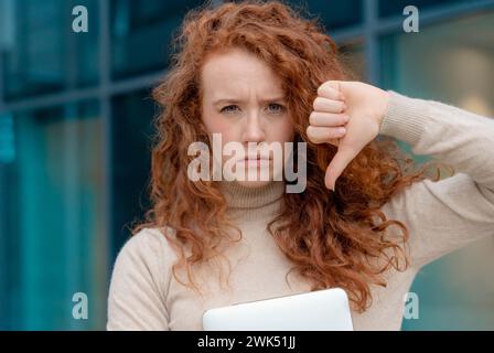 donna in maglione che dà un gesto con il pollice giù, non ama qualcosa, ha un'espressione disgustosa, mostra un segno di disapprovazione su sfondo blu. hu negativo Foto Stock