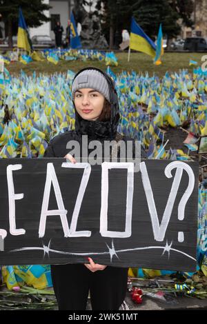 KIEV, UCRAINA - 18 febbraio 2024: Si vede una giovane donna con in mano un manifesto AZOV LIBERO sullo sfondo di un gran numero di bandiere ucraine con i nomi dei prigionieri e dei morti Foto Stock