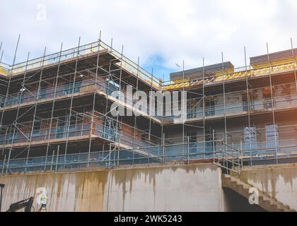 Ponteggi eretti intorno a una nuova casa in mattoni a più piani su un nuovo sito di sviluppo residenziale per consentire un accesso sicuro a un luogo di lavoro e windo Foto Stock