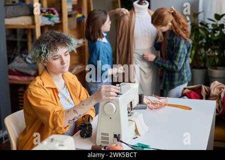 Vista laterale ritratto di una giovane donna con una protesi manuale che prepara la macchina da cucire in un'area di copia dell'officina dedicata alla classe sartoriale Foto Stock