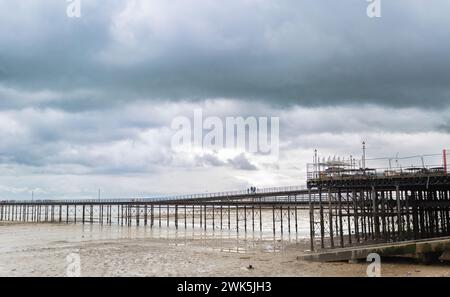 Figure sagomate distanti che camminano lungo la struttura del molo costiero. Foto Stock