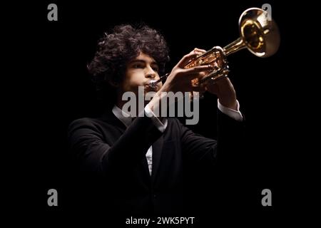 Giovane con una tuta nera che suona una tromba isolata su sfondo nero Foto Stock