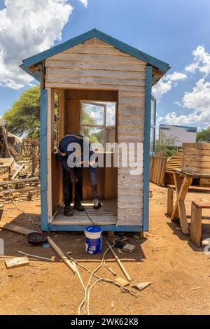 lavoratore afroamericano che realizza una casa wendy, capannone di legno all'aperto, sta usando una smerigliatrice angolare per levigare il pavimento Foto Stock