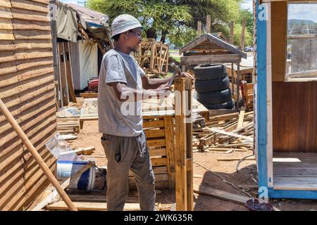 lavoratore afroamericano che costruisce una casa wendy, capannone di legno all'aperto, sta martellando un pallet per fare tavole Foto Stock