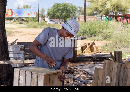 falegname afroamericano che crea una casa wendy, capannone di legno all'aperto, da vicino, sta macinando le tavole e assemblarle in pannelli Foto Stock