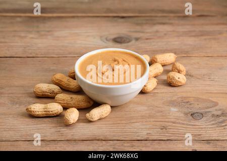 Delizioso burro di noci nel recipiente e arachidi su un tavolo di legno Foto Stock