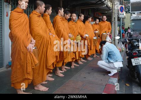 Durante il loro tradizionale giro di elemosina mattutina a Bangkok, Thailandia, un gruppo di monaci novizi di Wat Mahathat si allineano per dare benedizioni a un laico Foto Stock