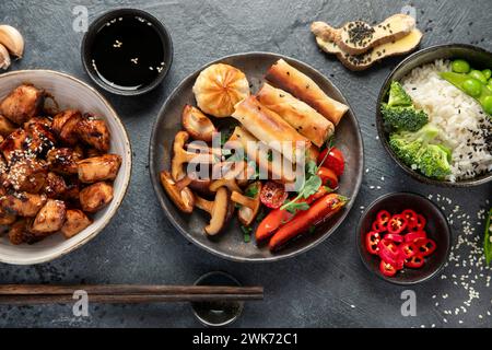 Teriyaki di pollo su sfondo scuro con salse, riso, verdure e semi di sesamo. Cibo asiatico. Vista dall'alto. Foto Stock