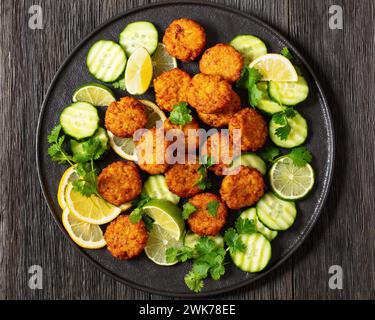 torte di riso fritte, tikki di riso, piatto indiano su piatto nero servito con cetriolo, limone, fette di lime su un tavolo di legno scuro, piatto, primo piano Foto Stock