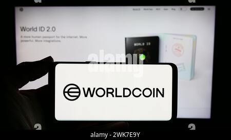 Persona con smartphone con logo del progetto di criptovaluta Worldcoin (Tools for Humanity) davanti al sito web. Mettere a fuoco il display del telefono. Foto Stock