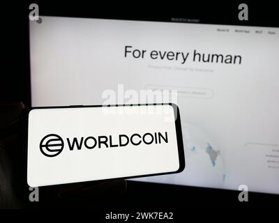 Persona che detiene un cellulare con il logo del progetto di criptovaluta Worldcoin (Tools for Humanity) di fronte alla pagina web aziendale. Mettere a fuoco il display del telefono. Foto Stock