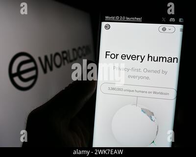 Persona che detiene un cellulare con pagina web del progetto di criptovaluta Worldcoin (Tools for Humanity) davanti al logo. Messa a fuoco al centro del display del telefono. Foto Stock