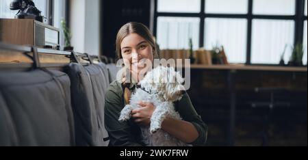 Ritratto di una bella giovane donna che tiene il cane e sorride. Carino cane bianco tra le braccia di amorevole proprietario. Con il cane nel bar. Foto Stock
