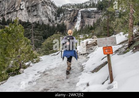 Escursione su un percorso invernale innevato e ghiacciato nel Parco Nazionale di Yosemite, nelle montagne della Sierra Nevada, California, verso una cascata nel paesaggio lontano. Foto Stock