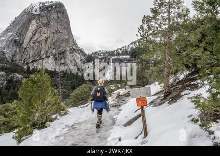 Escursione su un percorso invernale innevato e ghiacciato nel Parco Nazionale di Yosemite, nelle montagne della Sierra Nevada, California, verso una cascata nel paesaggio lontano. Foto Stock