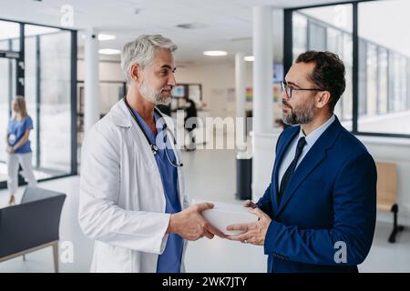 Rappresentante di vendita farmaceutico che presenta il nuovo farmaco al medico nell'edificio medico, che tiene e consegna la scatola con farmaci, campioni di farmaci a. Foto Stock