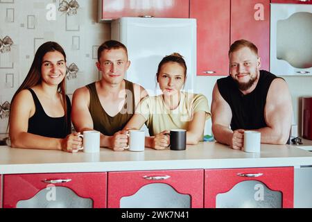 Due giovani famiglie trascorrono del tempo nella cucina della casa di campagna, le coppie sposate bevono il tè davanti all'isola della cucina, i giovani sorridono. Foto Stock