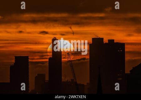 Londra, Regno Unito. 19 febbraio 2024. Il sole sorge sopra Canary Wharf e la City di Londra (come si vede da Primrose Hill), portando al cielo arancione prima che sparisca in bassa copertura nuvolosa. Crediti: Guy Bell/Alamy Live News Foto Stock