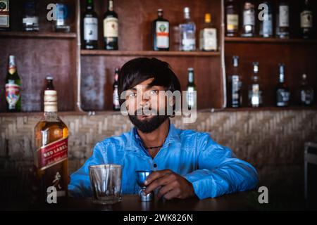 Bevande alcoliche, persone e concetto di professione - barman indiano a Goa India. Il bar si sta preparando a versare un drink nel bicchiere. Foto Stock