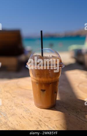 Vista ravvicinata di un caffè greco ghiacciato, noto anche come caffè frappe con una paglia in una spiaggia di iOS Grecia Foto Stock