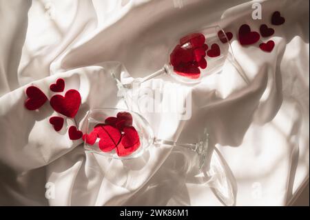 Bicchieri da vino con cuori rossi su un foglio bianco alla luce del sole Foto Stock
