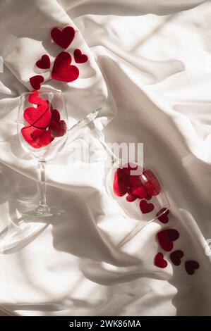 Due bicchieri da vino con cuori di tessuto su lenzuola bianche al sole Foto Stock