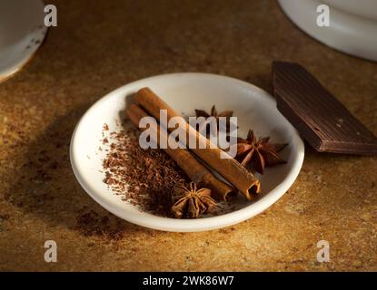 Bastoncini di cannella, anice e cioccolato fondente si trovano in un piatto sul tavolo Foto Stock