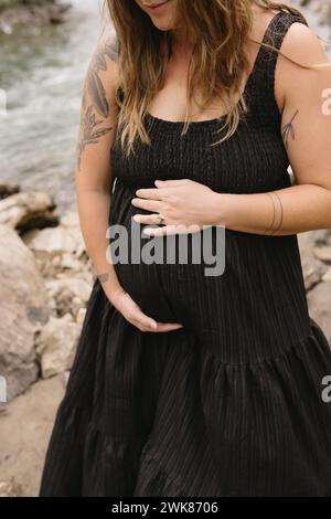 donna che tiene in braccio la pancia del bambino durante il servizio fotografico di maternità all'aperto Foto Stock